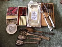 Overall view of the lot showing Sheffield carving set, steak knives in wooden holder, silverplate serving spoons, metal coasters, small decorative dish, and silverplate tray.