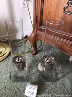 Set of two vintage oil lamps with glass square bases and tall clear chimneys on carpet floor.