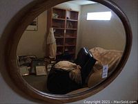 Oval mirror reflecting a room with shelving, furniture, and other household items, showing the wood grain frame and oval shape.