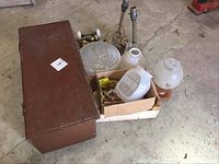 Wooden box closed with lighting fixtures, door knobs and other hardware beside it on floor