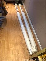 Two long rolled blinds on the floor in original clear wrap packaging showing dimensions 84" x 84" and brand information.