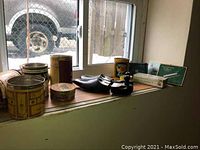 Overview of the vintage tins, cigarette cases, and shoe stretcher displayed on a wooden window sill with outdoor background visible.