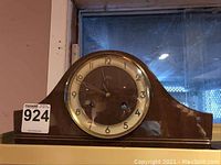 Full front view of the Solar mantle clock, showcasing its wooden case and glass clock face with Arabic numerals.