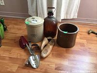 Photo showing full lot: beige Medalta crock with lid, brown glass bottle with handle, brown open crock, and three sets of wooden shoe stretchers