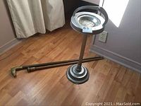 Photo showing the ashtray on stand and wood cane on floor next to wall outlet, natural lighting