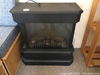 Full front view of black electric fireplace heater, showing front glass panel and artificial logs inside.