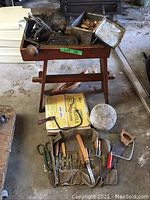 Overview photo showing the small wooden work bench, tools placed on the bench including two hand planers and manual drill, chisels on ground, wooden door knobs, and the large wooden round block.