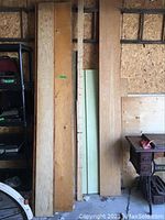 Vertical wooden planks alongside drywall and plywood sheets against a wall, showing different wood tones and textures