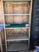 Metal utility shelving unit against wood wall with four particle board shelves and crossed support braces.