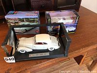 Photo of three car models/kits on wooden table showing assembled 1958 Cord 810 model with boxes for 1958 Chevy Impala and 1956 Ford Thunderbird behind