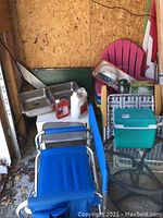 View showing miscellaneous patio lot items including Adirondack chairs, folding blue lawn chairs, double kitchen sink, cooler and other items in a garage area.