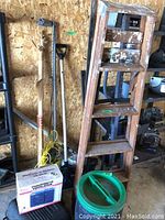 View showing the wood painter's ladder, shovel, electric heater box, dolly, and part of the utility shelf with various background items.