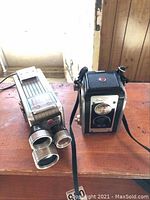 Overview of Kodak Brownie 8mm movie camera and Kodak Duaflex III camera side by side on a wooden surface.