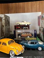Wide shot showing yellow Volkswagen Beetle, blue Opel GT, 1940 Ford Woody Wagon in box, and cream convertible with display case behind