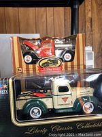 Two boxed trucks: red 40s Ford pickup with open hood and cream/green Liberty Classics tow truck