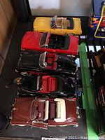 Five metal die cast model cars displayed on a black surface, showing different colors and convertible designs.