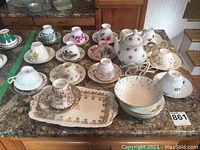 Wide view showing all teacups with saucers, serving tray, bowl, and electric teapot arranged on countertop.
