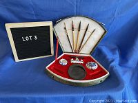 View of opened fan-shaped box with five brushes inserted upright, porcelain brush rest at center, two porcelain pots, and ink mixing stone arranged inside with red velvet lining