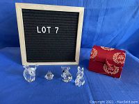 All four Swarovski crystal animal figurines and the red fabric case on blue background beside a letter board showing lot number.