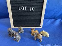 Photo showing all six animal figurines: three pewter (dog, rabbit, owl) and three stone (two rabbits and elephant) on a blue fabric background and a letter board reading LOT 10.