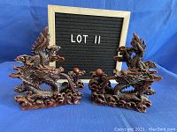 Two red-tinged ornate dragon sculptures displayed side by side in front of a sign reading 'LOT 11' on a blue background.