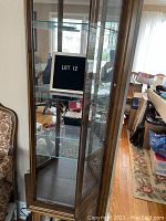 Full view of the curio cabinet showing front glass doors, wooden frame, and interior glass shelves with mirrored back.