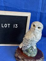 Snowy owl figurine on separate wooden base against blue backdrop with LOT 13 sign