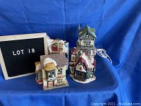 Four assorted porcelain/ceramic Christmas village buildings grouped on blue fabric background showing varied architecture and snow-covered roofs.