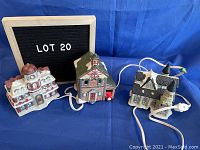 Three connected porcelain ceramic Christmas village buildings: Church, Firehall, Victoria Station with wiring for lights, shown from above on a blue cloth background.