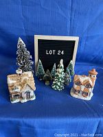 Front view of Christmas village lot with two houses and six evergreen trees arranged on blue fabric background