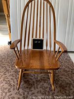Front view of the wooden Windsor back rocking chair showing the seat, arms, and spindled backrest.