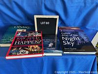 Five hardcover books displayed on a blue cloth including an Atlas, Chris Hadfield book, How Did It Really Happen?, National Geographic and Life books.