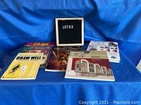 Six books on a blue cloth background arranged in two rows with a sign reading LOT63 in the background