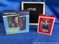 Photo showing both unopened figure boxes: Piper Wright from Fallout Crate and Elizabeth from Bioshock Infinite, set against a blue cloth background with a lot number sign.
