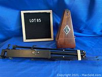 Wooden metronome and folded extendable metal music sheet stand placed on blue cloth background with Lot 85 board.