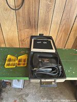 Black & Decker two speed electric jigsaw in case with two yellow blade holders next to it on a green table with wooden panel background.