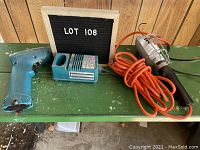 Photo of Makita 6010 cordless drill body, battery charger and work light with orange extension cord on green table, marked lot 108