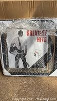 Framed record cover wrapped in protective bubble wrap, showing 'Greatest Hits' album cover insert for display demonstration.