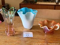Overview of three glass art vases on wood surface as part of the lot.