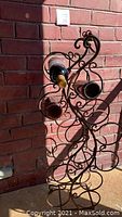Photo showing the wine rack holding several wine bottles, illustrating its rustic cast iron design and scrollwork pattern.