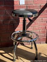 Bar stool with black round leather seat, chrome legs with rubber stoppers, circular chrome foot rest, and hydraulic lift at different height positions.