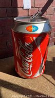 Angle view of Coca-Cola cooler in shape of a can, showing its red and silver body with Coca-Cola script, and temperature indicator on top.