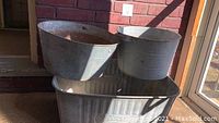 Set of three tin tubs grouped together outside on porch area with sunlight and shadows cast, showing size and shape differences.