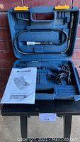 Open blue plastic carrying case containing a blue Mastercraft rotary tool with power cord, flexible shaft attachment secured in upper lid compartment, and instruction manual.