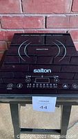 Top-down view of the induction cooktop showing the brand name 'Salton', induction cook surface with caution text, and touch controls at front.