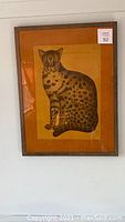 Full view of one framed Ocicat wild cat print showing brass and wood frame with orange matte background and clear glass.