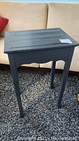 Front view of black painted vintage pine side table with rectangular top and four legs.