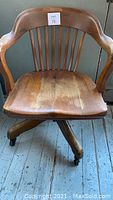 Front view of vintage oak swivel bankers chair with curved back and armrests on caster base.