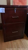 Two drawer wood filing cabinet with brass-like handles and key inserted in lock on top drawer.