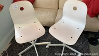 Pair of white Ikea Vagsburg Sporren chairs side by side on carpet with beige sofa background